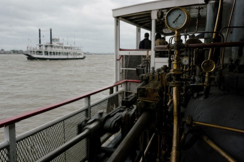 Polished brass steam gauges and levers in a riverboat engine room with pistons moving behind a safety rail