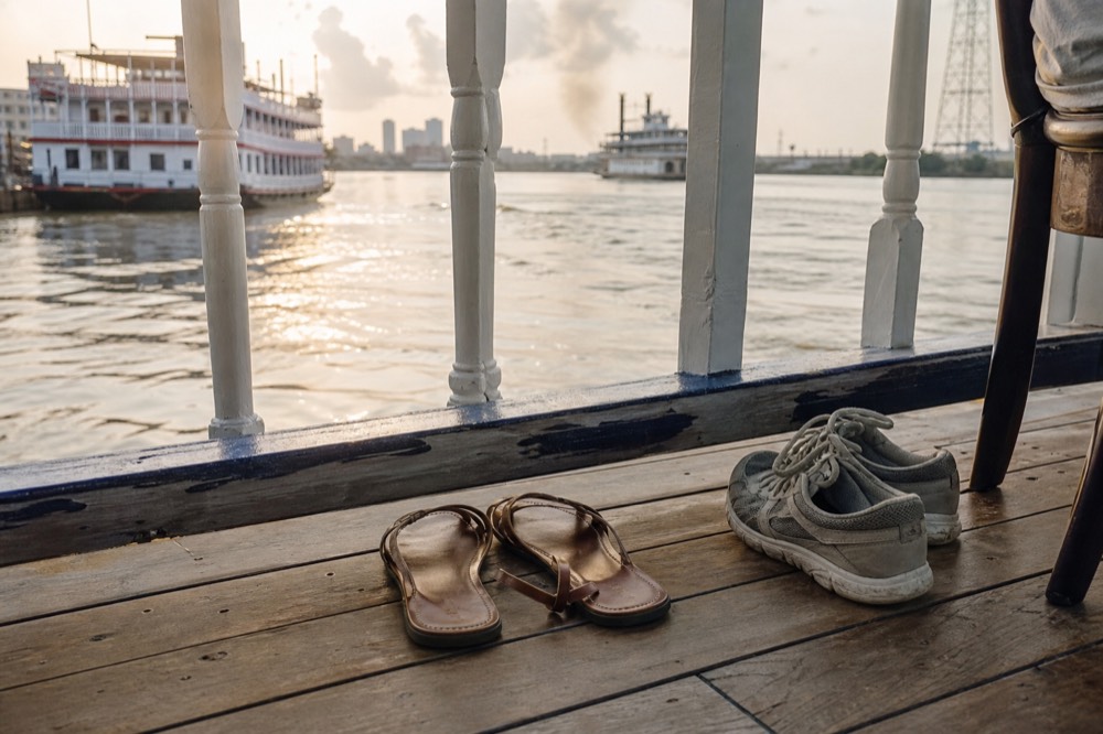Close view of flat leather sandals and trainers on a wooden riverboat deck beside a white painted railing