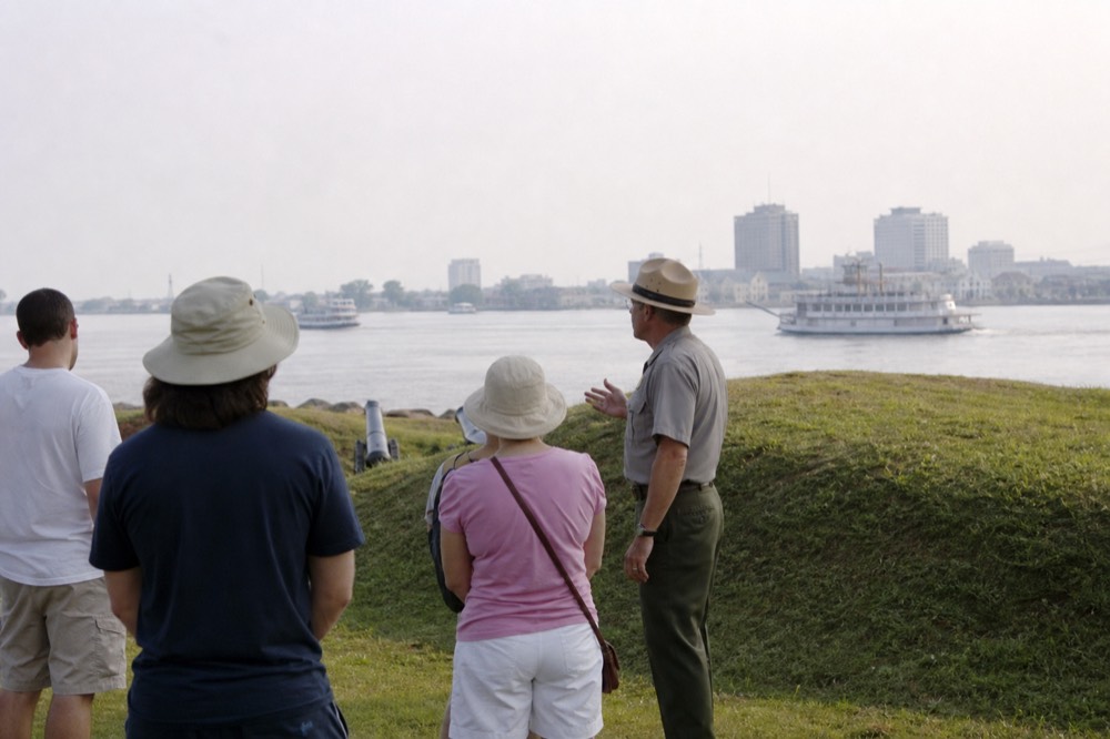 Park ranger in uniform speaking to a small group of visitors beside an earthen rampart on an open battlefield lawn