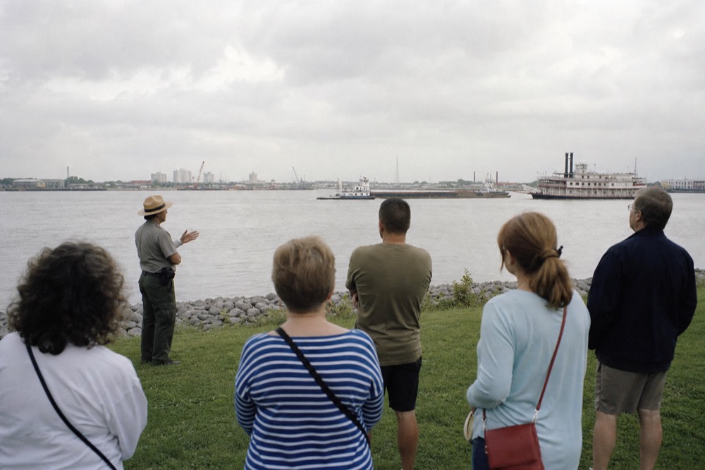 A small group of visitors standing on open battlefield grass listening to a uniformed park ranger with a flat-brimmed hat