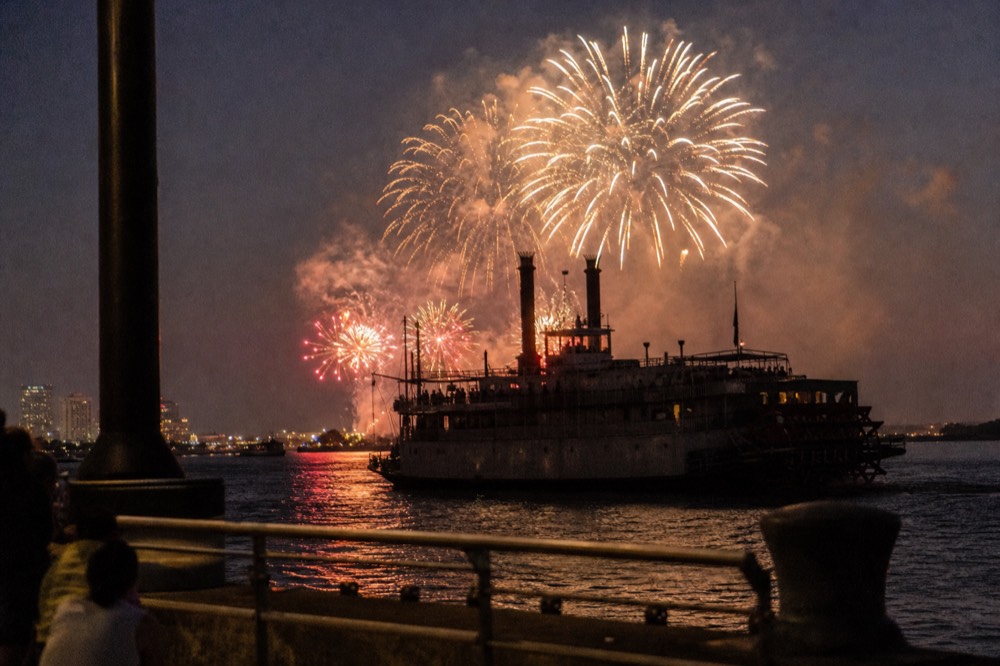 Fireworks bursting over the Mississippi River with a paddlewheeler silhouetted in the foreground