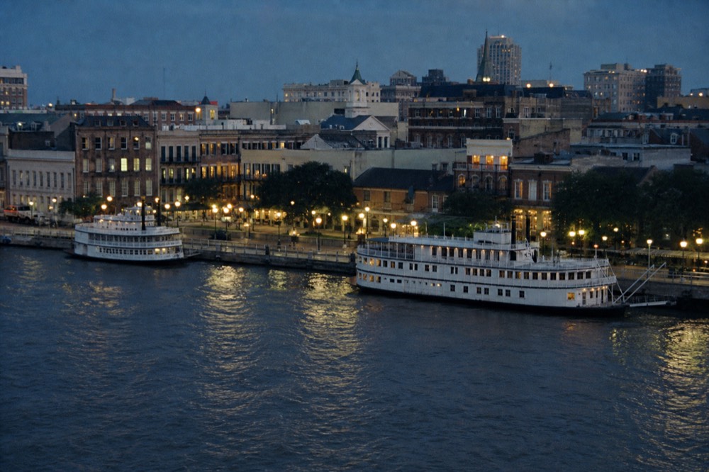 Two white excursion riverboats moored a block apart along the New Orleans riverfront with the French Quarter rooftops behind them