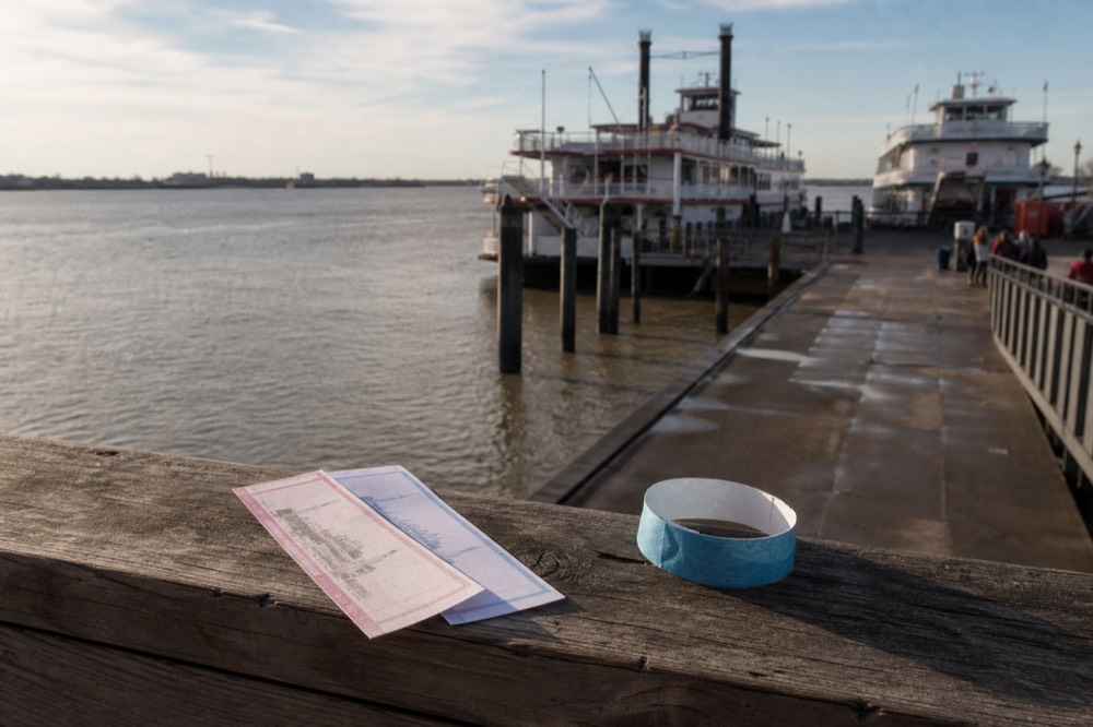 Printed riverboat boarding tickets and a paper wristband resting on a wooden dock rail beside the Mississippi