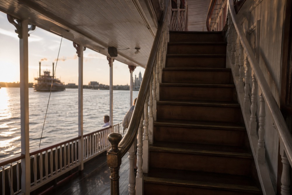 Steep varnished wooden staircase connecting two decks of a historic riverboat, brass handrail worn smooth