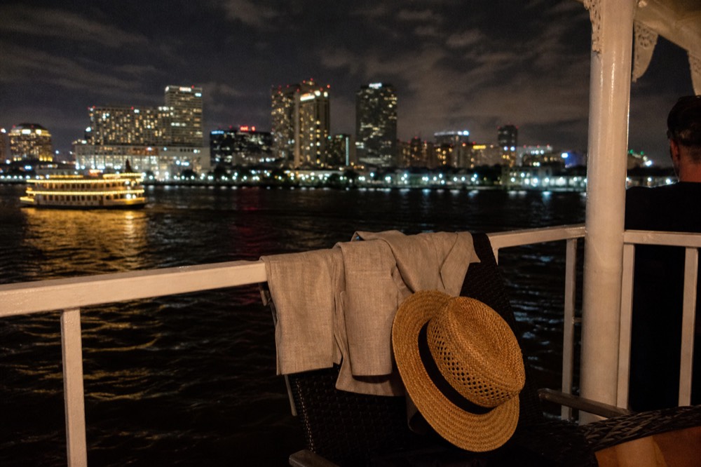 A folded light linen jacket and a straw hat resting on a riverboat deck chair with sunlight on the white railing behind